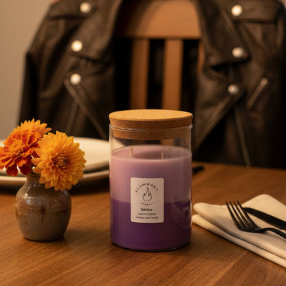 Purple candle in a glass jar with wooden lid on a table with flowers and cutlery.